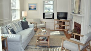 A living room with a white sofa, striped armchairs, a coffee table with magazines, a TV, and a fireplace. - Beautiful,  updated 3 bedroom home with parking for 6 cars in downtown Newport (Newport)