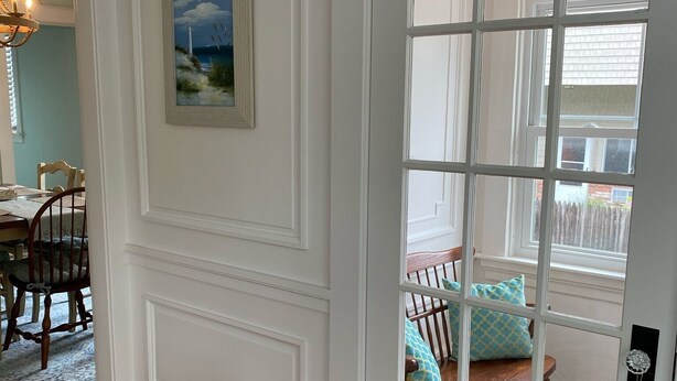 A room with a white paneled door, a wooden floor, a dining area with a table and chairs, and a view through a glass door into another room with a bed and pillows. - Beautiful,  updated 3 bedroom home with parking for 6 cars in downtown Newport (Newport)