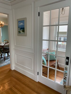 A room with a white paneled door, a wooden floor, a dining area with a table and chairs, and a view through a glass door into another room with a bed and pillows. - Beautiful, updated 3 bedroom home with parking for 6 cars in downtown Newport (Newport)