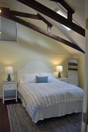 Une chambre à coucher avec un lit, deux tables de chevet avec des lampes, une fenêtre et une poutre en bois au plafond.