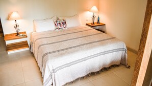 Un lit bien fait, recouvert d’une couverture à rayures, deux tables de chevet avec des lampes et un coussin coloré.