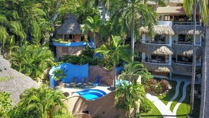 A resort with a swimming pool, thatched-roof structures, and lush greenery.