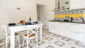 A compact kitchen with white cabinets, a tiled backsplash, and a dining area with a white table and chairs. - Angolo di Paradiso (Vico Equense)