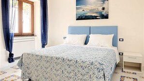 A bedroom with a bed, a window with curtains, a painting on the wall, and a tiled floor. - Angolo di Paradiso (Vico Equense)