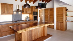 A modern kitchen with wooden cabinets, a central island, pendant lighting, and a built-in oven.