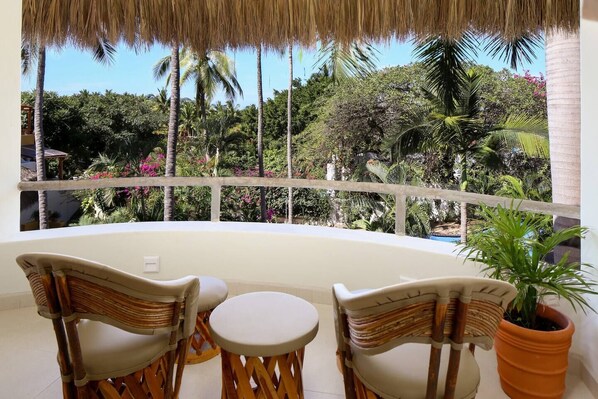 Enjoy a serene garden view from this balcony with a wicker chair and table.
