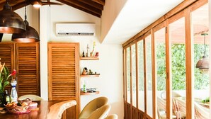 Um quarto espaçoso com teto de madeira, uma janela grande, um bar de madeira e um espaço de estar com cadeiras e banquinhos.