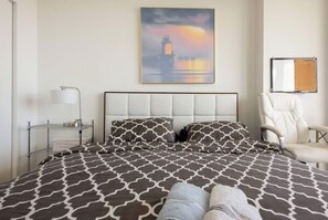 Une chambre d’hôtel avec un lit, une chaise, un tableau, une étagère et un tableau d’affichage.