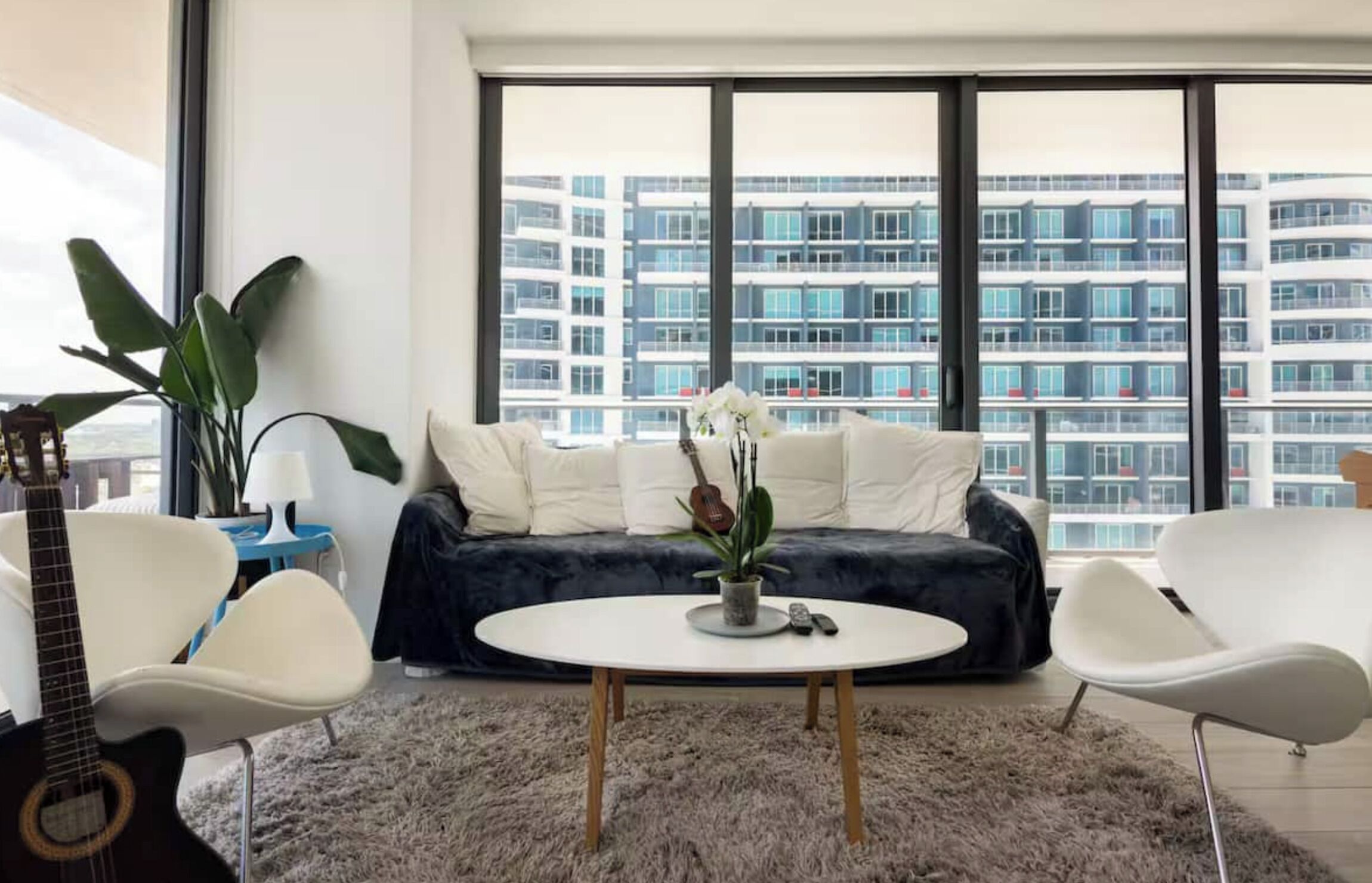A modern living room with a round coffee table, a sofa, and a large window offering a view of high-rise buildings.