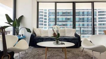A modern living room with a round coffee table, a sofa, and a large window offering a view of high-rise buildings.