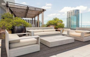 A rooftop terrace with outdoor seating, potted plants, and a view of a cityscape.