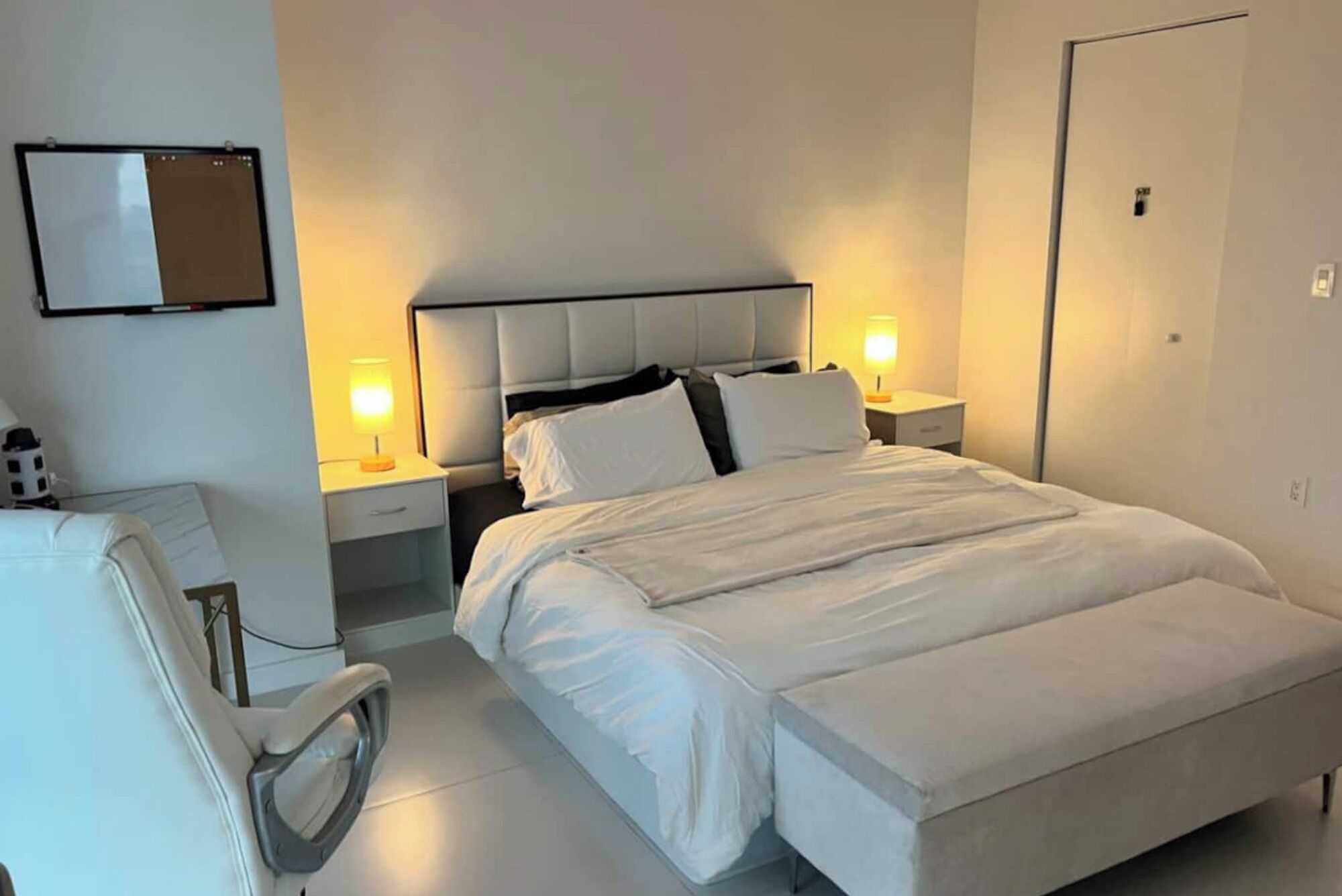 A hotel room with a bed, bedside tables, a chair, and a flat-screen TV.