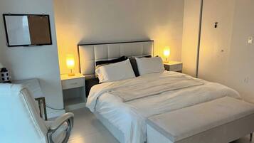 A hotel room with a bed, bedside tables, a chair, and a flat-screen TV.