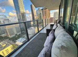 A balcony with a sofa, a glass railing, and a city view.