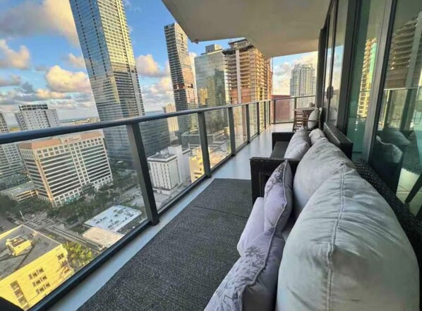 Un balcon avec un canapé, une rambarde en verre et une vue sur la ville.