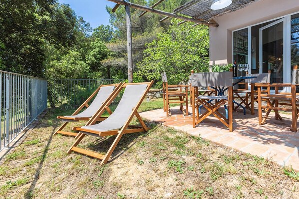 A patio with wooden chairs and a table, a pergola, and a view of a forested area.