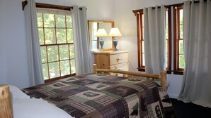 Ein Schlafzimmer mit einem hölzernen Bett, einem Schminktisch, einem Spiegel und zwei mit Vorhängen versehenen Fenstern.
