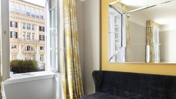 A room with a large window, a dark sofa, and a mirror on the wall.