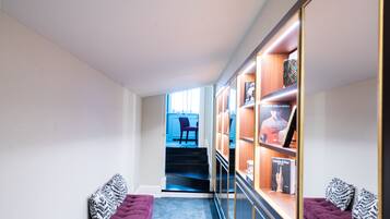 A hallway with a purple bench, a staircase leading to a blue room, and a display cabinet with books and a framed picture.