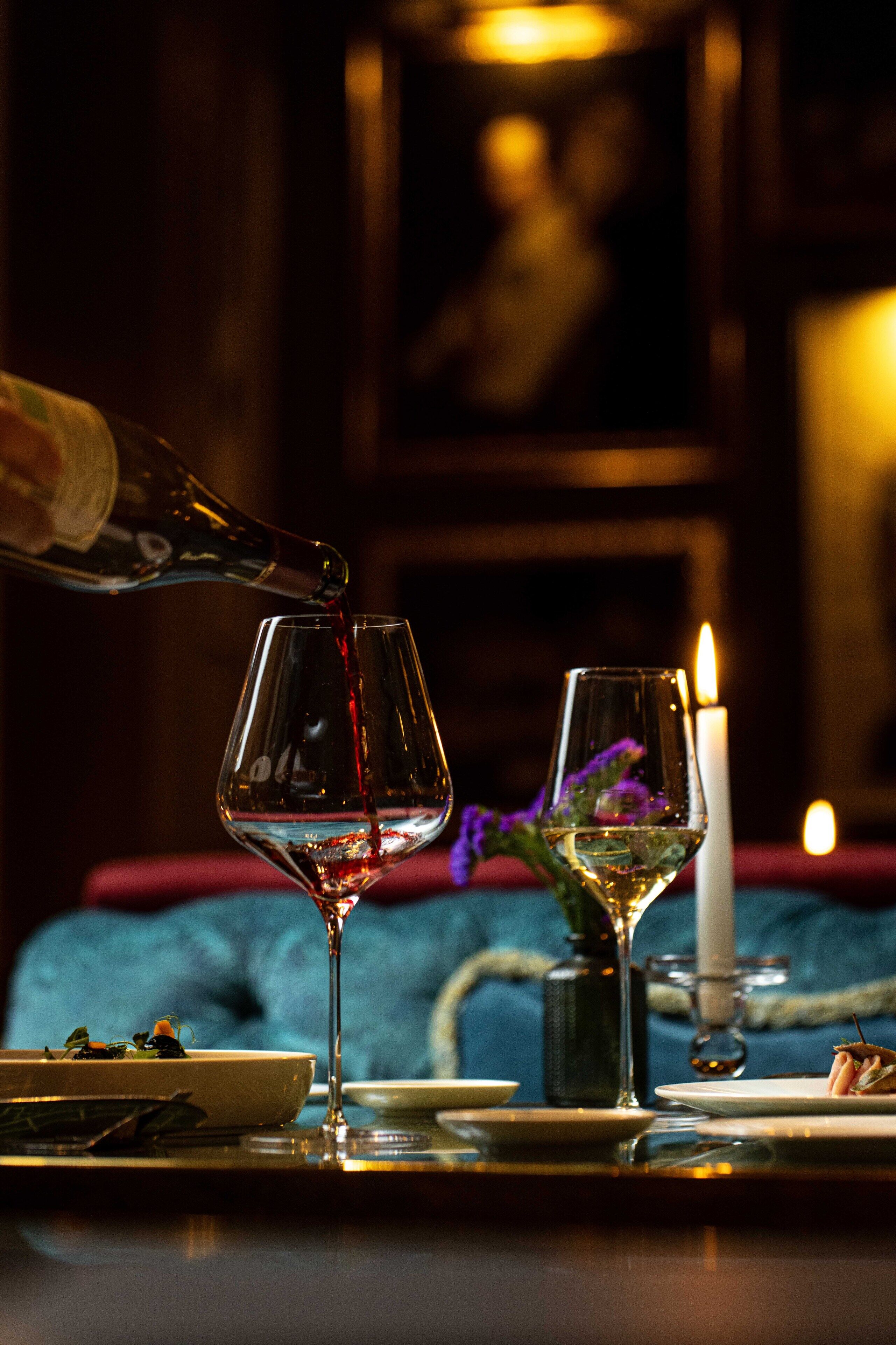 Una mesa de comedor con dos copas de vino, una vela y una botella de vino sirviéndose.