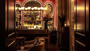 Zona de bar con suelo de madera, barra y área de asientos con sillas.