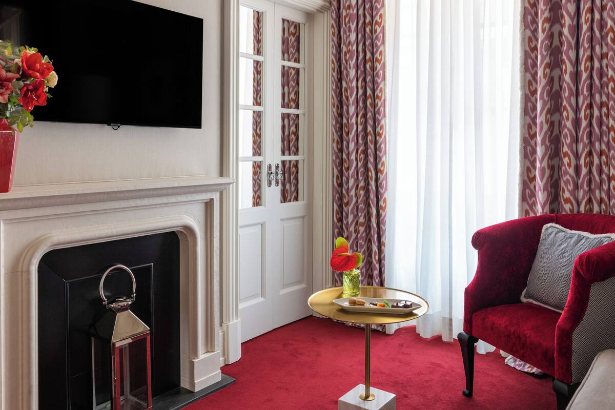 A room with a fireplace, a red armchair, a small table with a vase of flowers, and a television mounted on the wall.