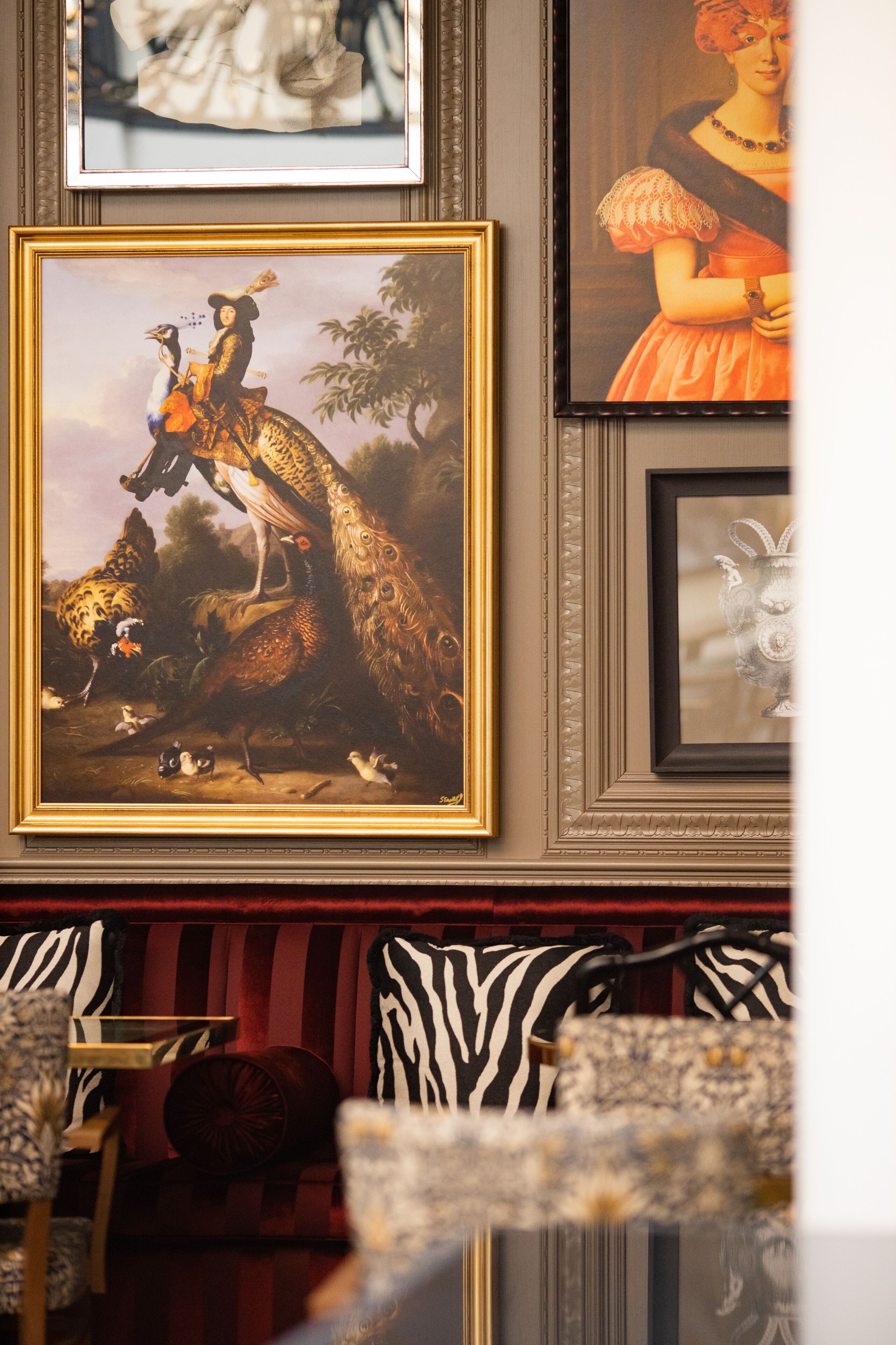 A framed painting of a man on a horse with a bird, a framed portrait of a woman, and a zebra-patterned couch.