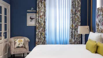 Een slaapkamer met een bed, een stoel, gordijnen, een spiegel en een foto aan de muur.