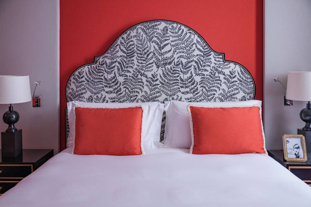 A neatly made bed with white and red bedding, a patterned headboard, and two bedside lamps.