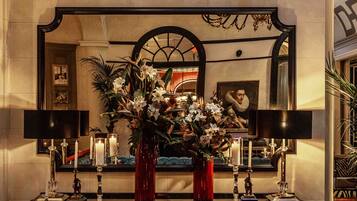 A dining area with a table set for two, a vase of flowers, candles, and a large mirror above the table.