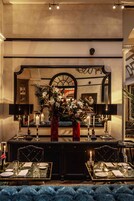 A dining area with a table set for two, a vase of flowers, candles, and a large mirror above the table.