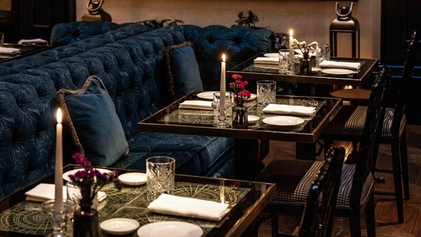 Comedor con un mural grande, un sofá tapizado en azul y una mesa dispuesta para cuatro personas con velas y copas.