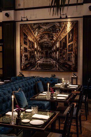 A dining area with a large mural, a blue upholstered sofa, and a table set for four with candles and glassware. - Maalot Roma (Rome)
