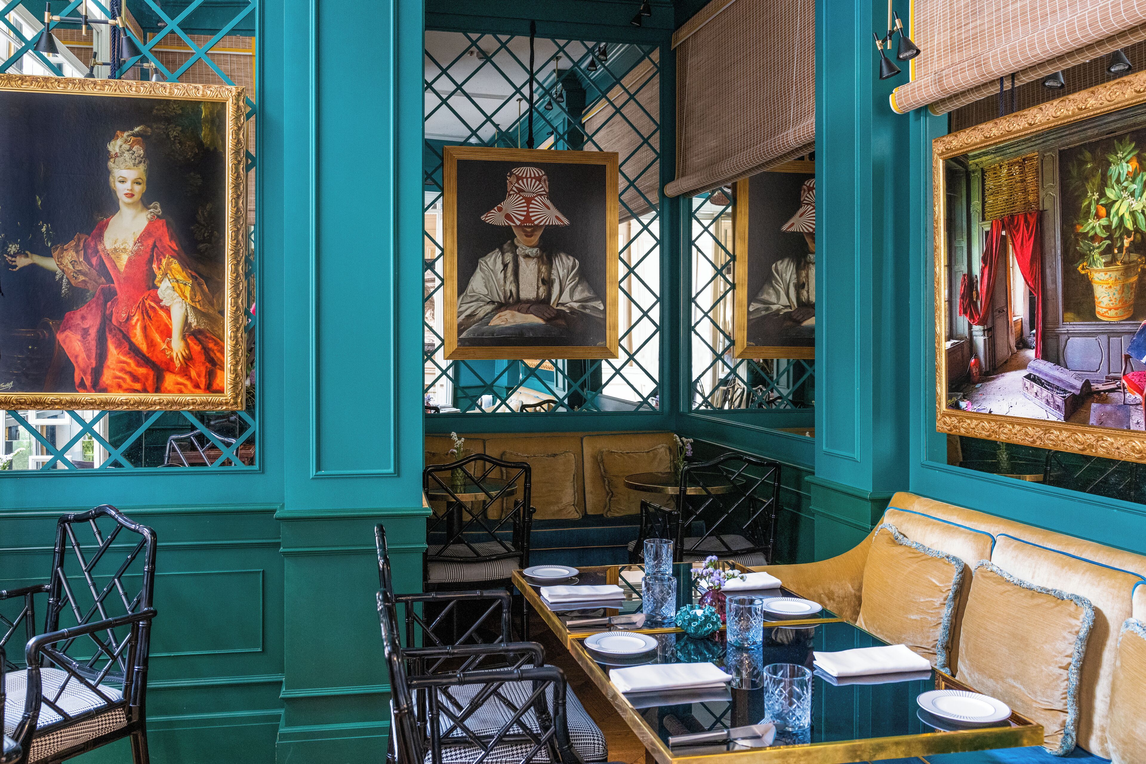 A dining area with a long table set for two, chairs, and framed artwork on the walls.