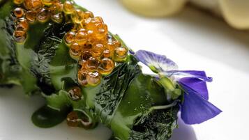 A plate with a green vegetable topped with orange beads and a purple flower, and a white object in the background.