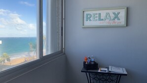 Une pièce dotée d’une grande fenêtre donnant sur la plage, d’un panneau encadré sur lequel on peut lire « DÉTENTE au bord de la mer », et d’une petite table avec des bouteilles d’eau et un menu.