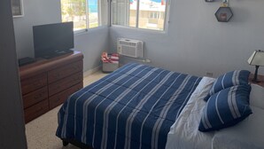Une chambre à coucher comprenant un lit, une commode, un téléviseur, un radiateur et une fenêtre donnant sur l’océan.
