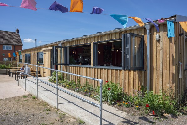 A wooden building with a metal railing, a garden with colorful flowers, and a clear blue sky. - 1 Bed Shepherds Hut - Sleeps 2 -wood Fired Hot Tub (Wincanton)