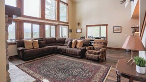 A spacious living room with a large sectional sofa, a patterned rug, and a dining area in the background. - Your Own Private Idaho for Summer Mountain Retreat (New Meadows)