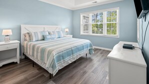 Een slaapkamer met een bed, nachtkastjes, een plafondventilator, een raam met zonwering en een televisie op een dressoir.