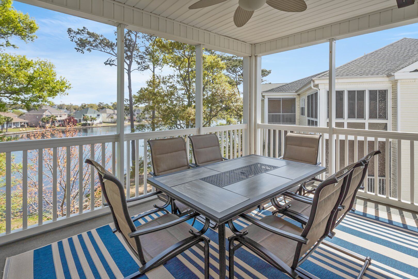 A covered outdoor patio with a table and chairs, overlooking a body of water and neighboring houses.