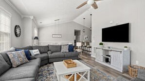 Een moderne woonkamer met een hoekbank, een witte salontafel, een open haard en een aan de muur bevestigde televisie.