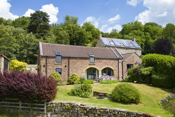 A stone building with a tiled roof, solar panels, and a garden with various plants and a seating area. - Five Acres, Boltby, North York Moors (Thirsk)