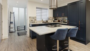 Una cocina moderna con armarios oscuros, una isla central con taburetes de bar y una campana extractora de acero inoxidable.
