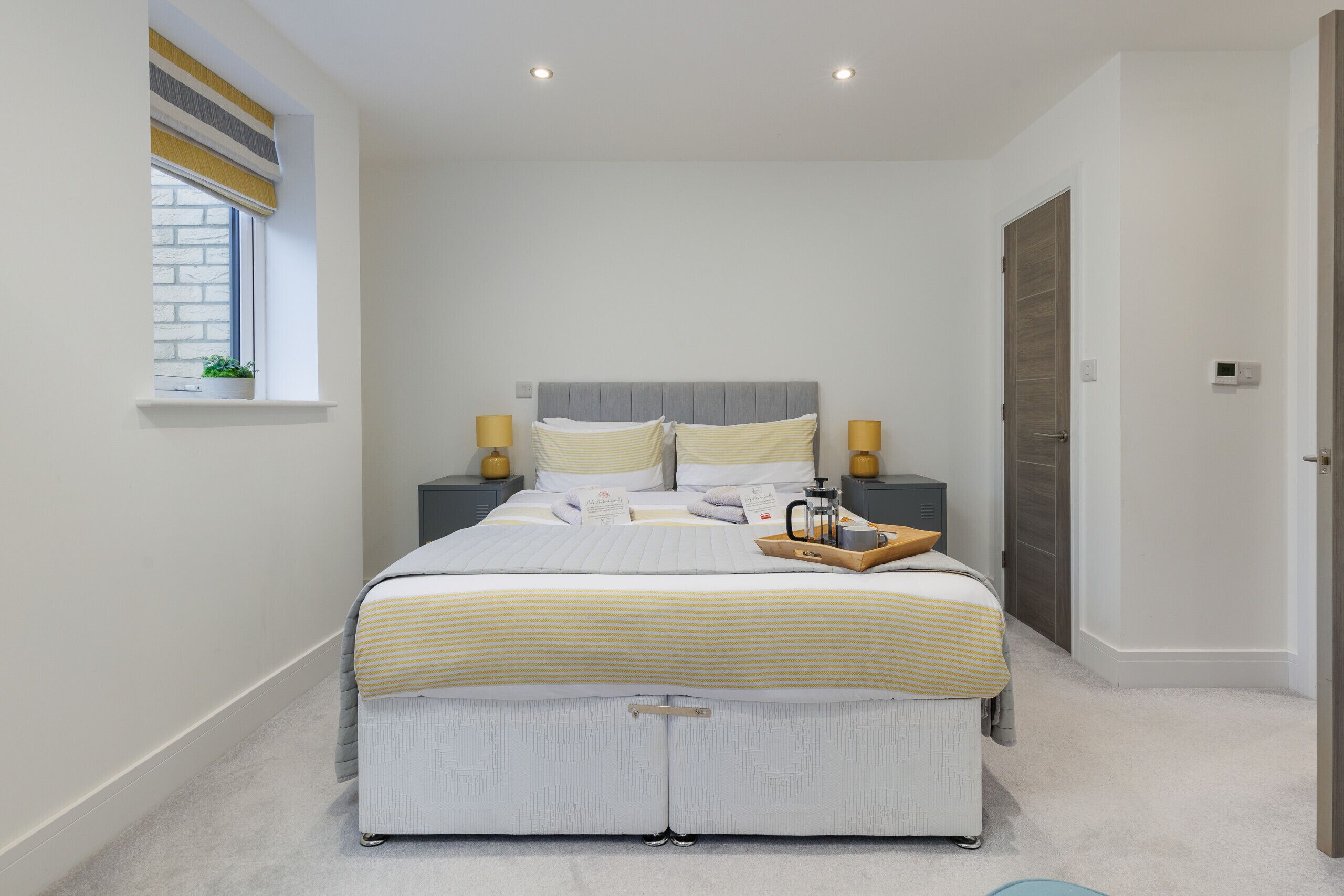 Een moderne slaapkamer met een bed, nachtlampjes, een raam met een plant en een deur.