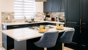 Una cocina moderna con armarios oscuros, una isla central y dos taburetes de bar.