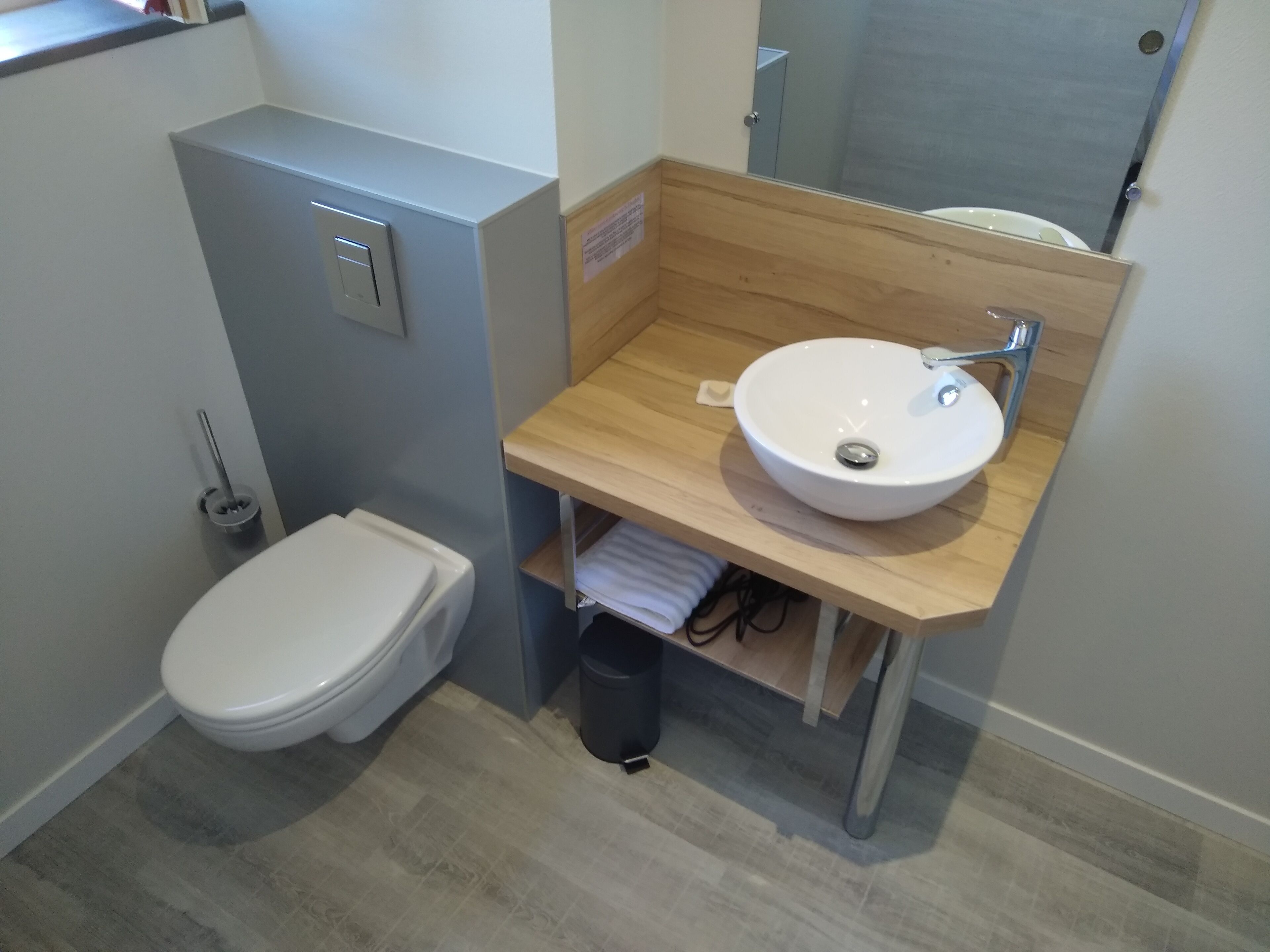 Une salle de bain moderne avec des toilettes blanches, un meuble-lavabo en bois avec un lavabo blanc et un miroir au-dessus du lavabo.