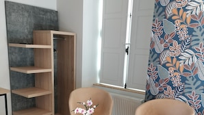 A modern room with a wooden floor, a large window, a white radiator, a blue patterned curtain, and two chairs with a small table between them. - Malicorn' Appart-hôtel (Malicorne-sur-Sarthe)