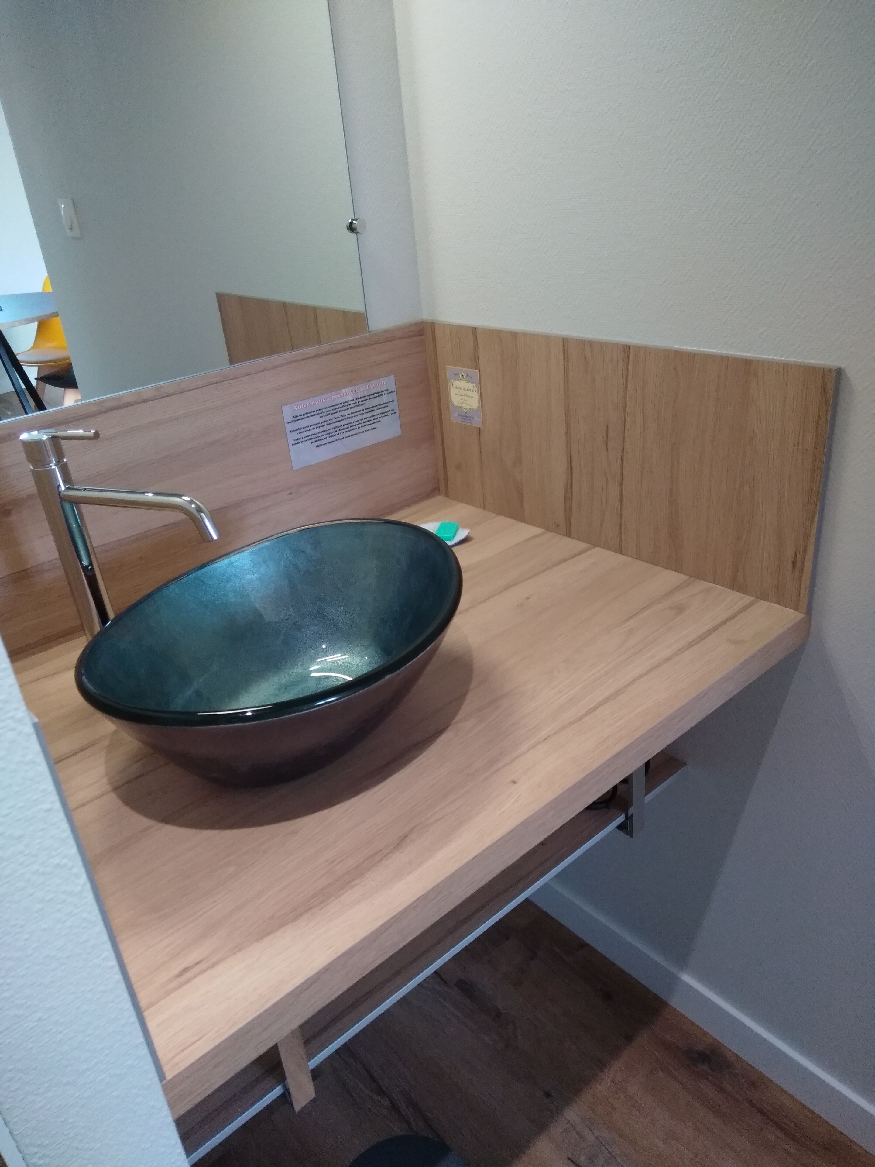 Een badkamer met een houten wastafelmeubel, een roestvrijstalen wastafel en een spiegel.