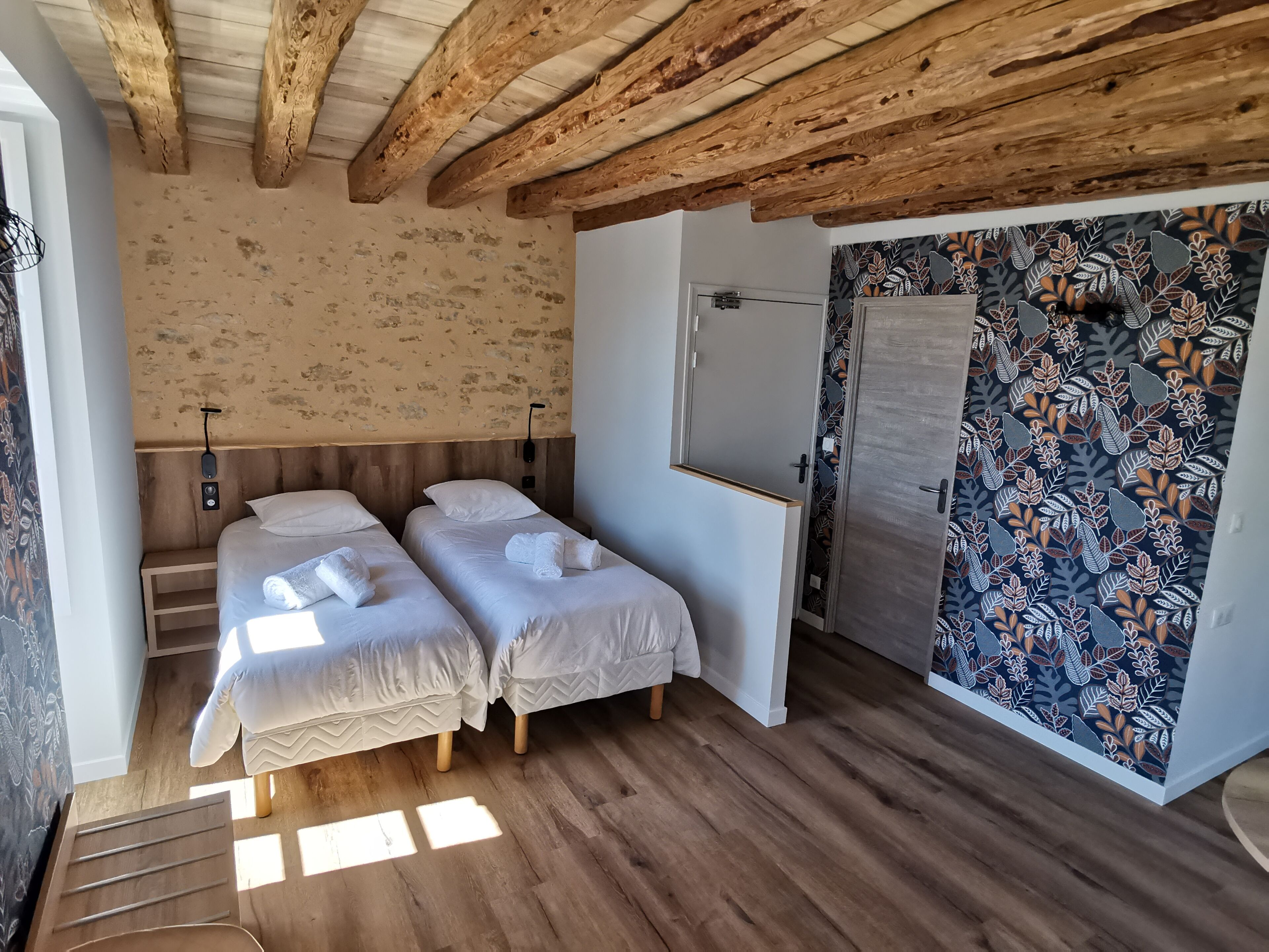 A room with two beds, wooden beams on the ceiling, a patterned wall, and a door.